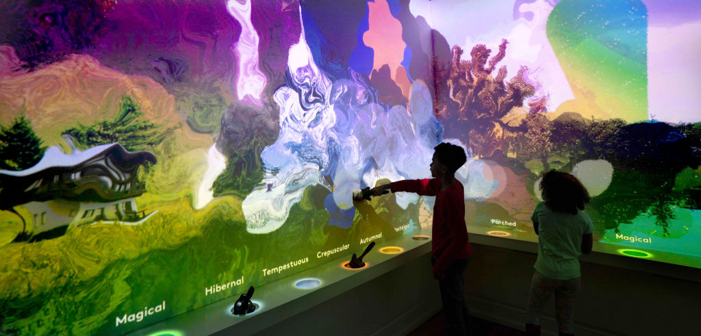 Two children in the Word Worlds exhibit at Planet Word. The wall is awash with swirls of color.