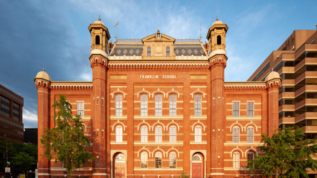 The front facade of the Planet Word building. It is a historic red brick building with decorative windows, cupolas, and a mansard roof.